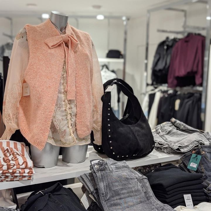 Gilet rose poudré et sac noir clouté en boutique